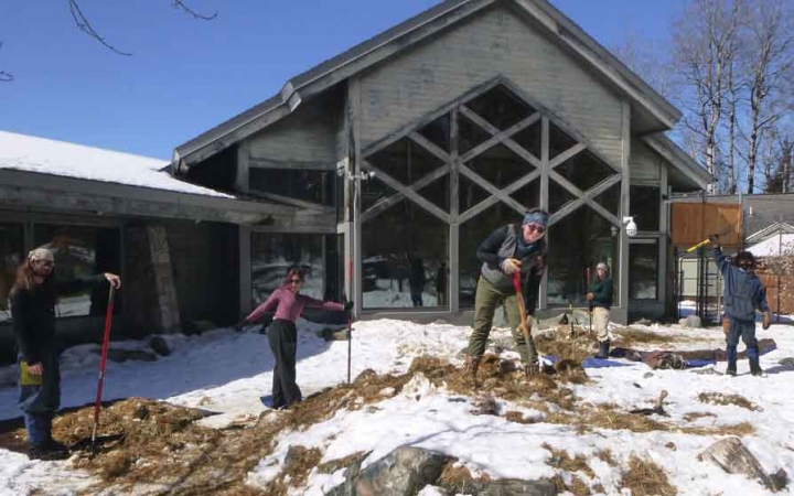 a group of students holding garden tools work on a piece of land in front of a building during a service project with outward bound